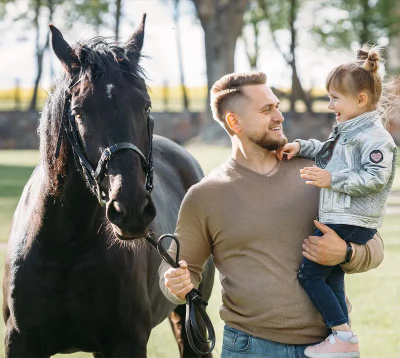 father holding his daughter next to a horse