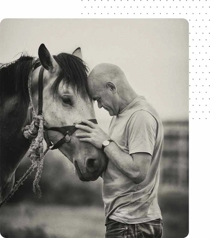 man resting his head on a horse's head in black and white